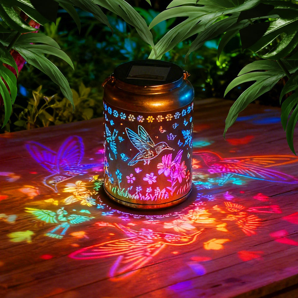 Dellicasi hummingbird solar lantern with gold-bronze finish emits a warm glow outdoors.
