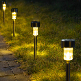 GIGALUMI solar pathway light in stainless steel illuminating a garden path at dusk