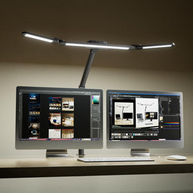 Honeywell wide desk lamp illuminates dual monitors with even lighting across the desk