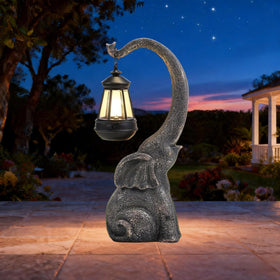 IVCOOLE solar elephant statue with nose lantern illuminating the garden at night.