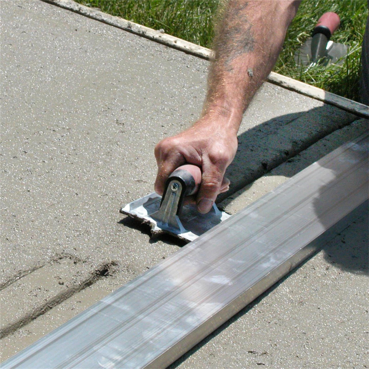 Zinc blade smooths across rough concrete to reveal crisp groove lines.