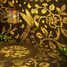 Miggley hummingbird projection lantern at night for cozy patios and pathways.
