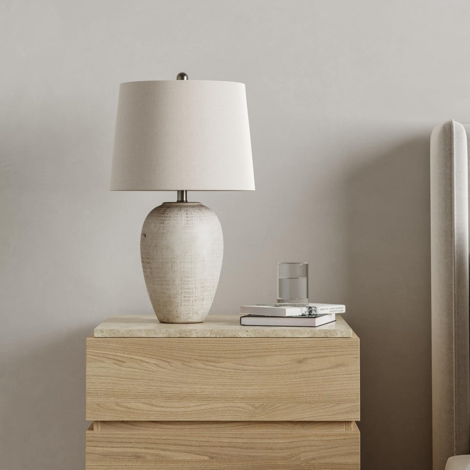 Nourison Home 23-inch distressed cream ceramic jar table lamp on nightstand provides warm ambient light.