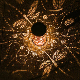 TIGGSY dragonfly lantern projects patterned light on garden walls at dusk