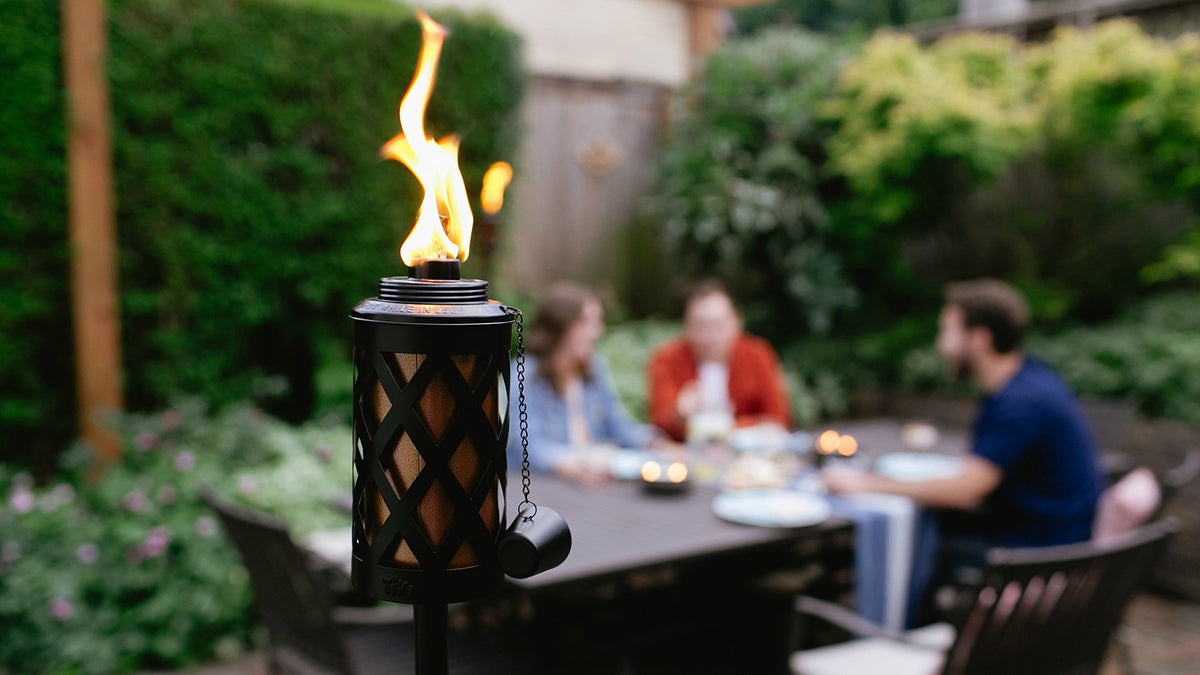 Outdoor scene with TIKI torches and weather-resistant canisters creating warm ambiance.