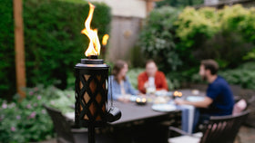 Outdoor scene with TIKI torches and weather-resistant canisters creating warm ambiance.
