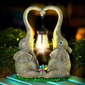 Vereemy elephant statue pair in a garden with a hanging lantern for warm outdoor ambiance.
